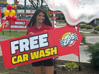 Woman holding "Free Car Wash ZIPS Car Wash" sign, smiling in front of newly remodeled ZIPS Car Wash location